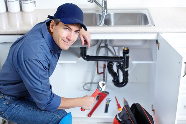 Plumber holding wrench with cabinets under sink open - Boyd Plumbing
