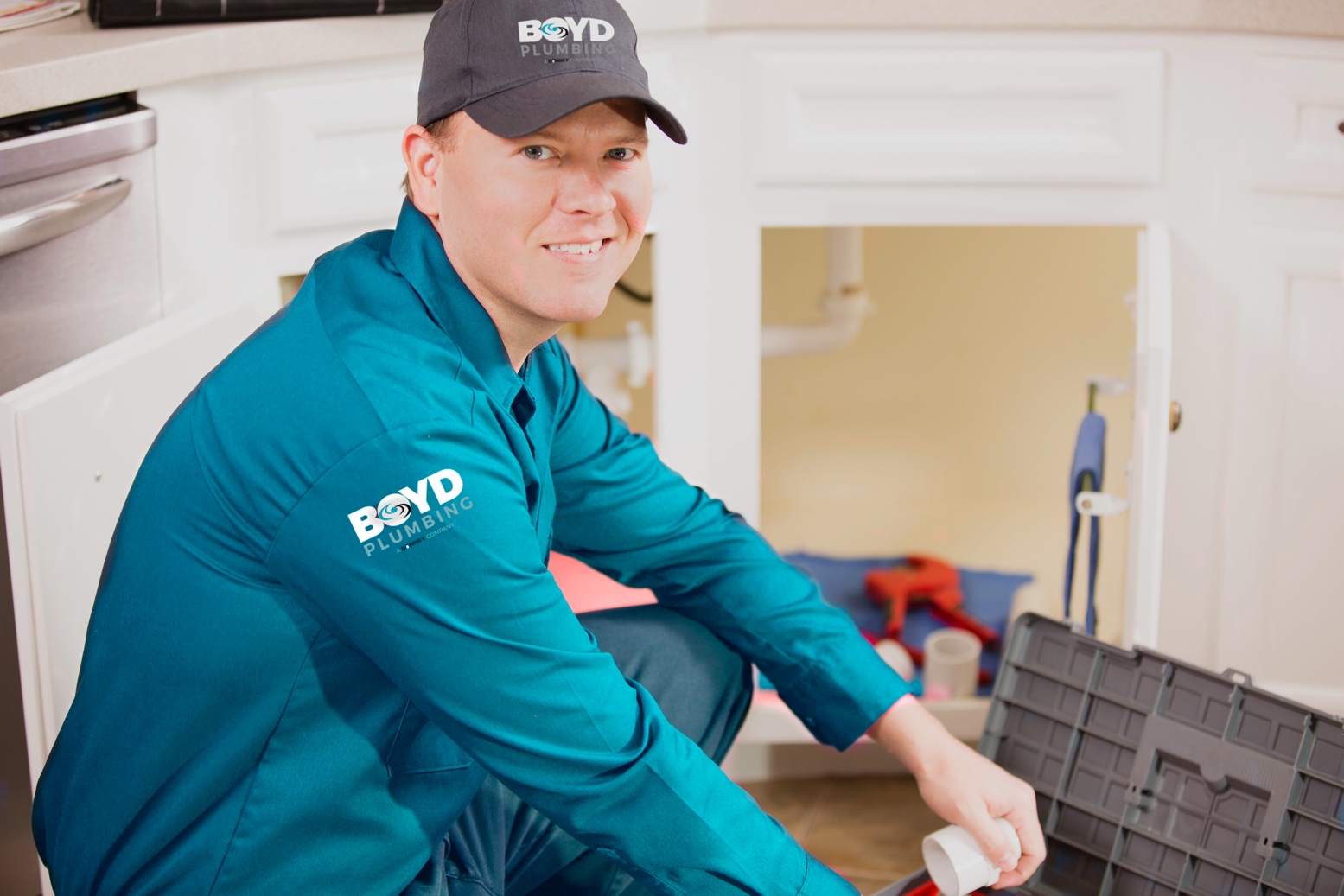 Boyd Plumbing technician smiling at camera while working under a kitchen sink - Boyd Plumbing